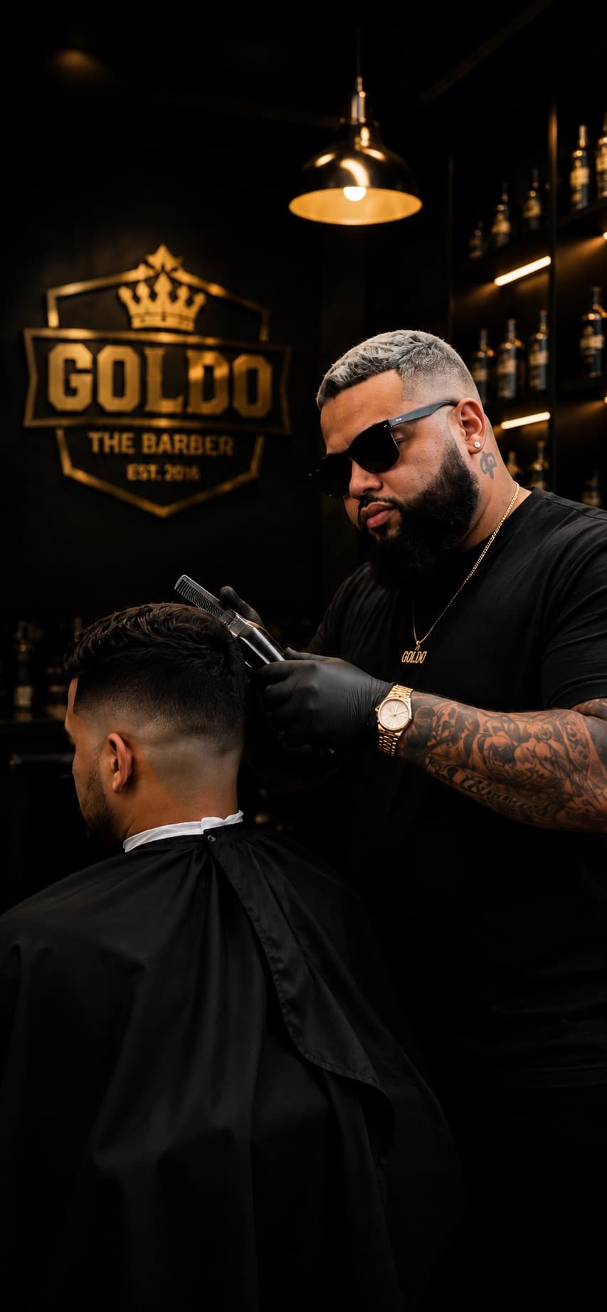 Goldo, a professional barber dressed in black, cutting a client's hair in a premium dark barbershop